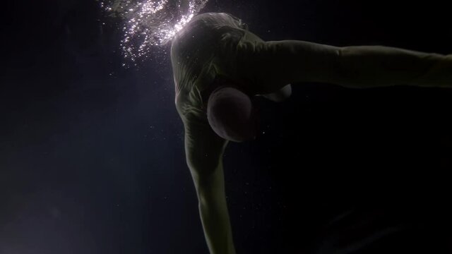 adult man is swimming in sea, ocean or river, underwater shot of dressed male figure in darkness