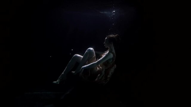 amazing underwater shot of floating woman in deepness and darkness, mysterious slow motion