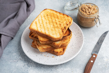 Bread toast crispy for sandwiches on a plate on a gray concrete table. A jar of chicken pate.