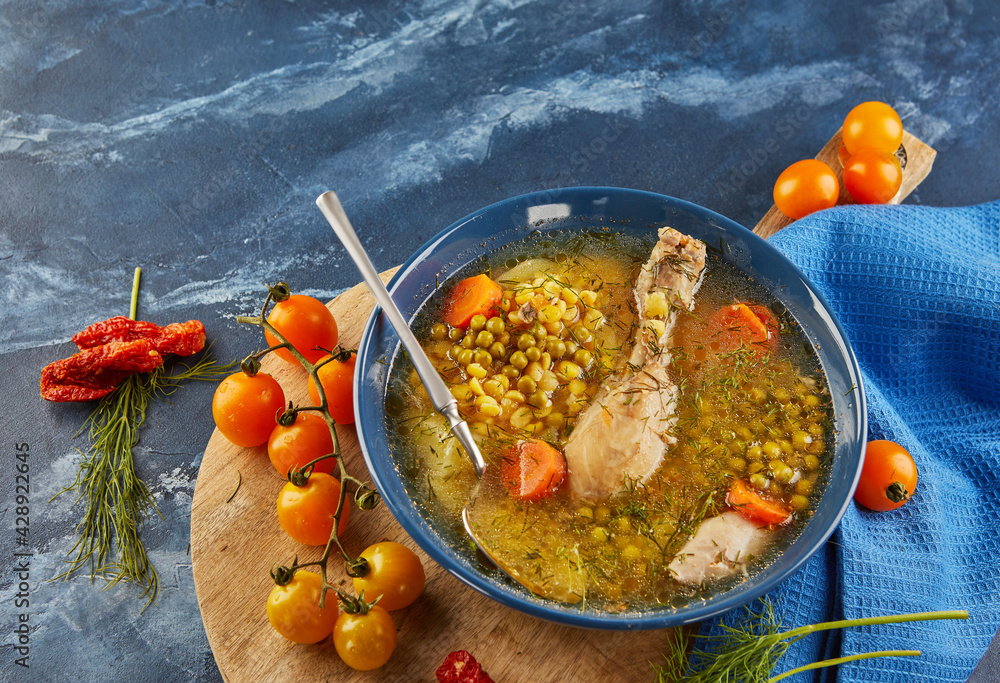 Wall mural Pea soup with chicken, carrots, tomatoes and herbs in a deep plate on wooden board with napkin on blue background