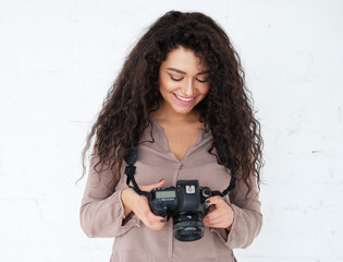 Portrait of Afican woman holding digital photocamera and laughing over white background in studio.