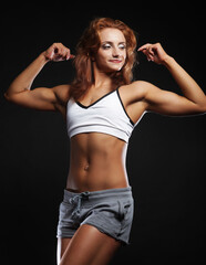 Photo of cheerful young red haired woman dressed sportwear over black background.