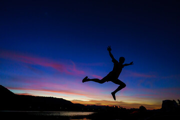 man Happy jump with his hands up during sunset at the lake or river, freedom concept