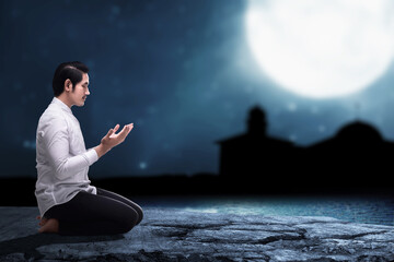 Asian Muslim man sitting while raised hands and praying