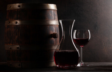 Wine decanter, glass of red wine and old wooden barrel