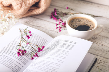 Book with fresh flowers and cup of coffee on table