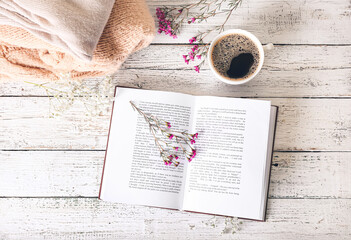 Book with fresh flowers and cup of coffee on table