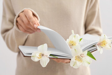Obraz na płótnie Canvas Woman holding book with fresh flowers, closeup