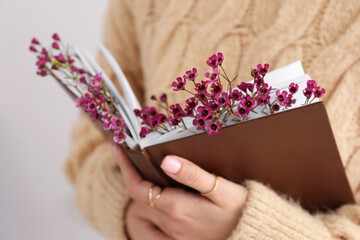 Woman holding book with fresh flowers, closeup