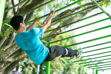 a muscular man in gym clothes doing hand exercises perfect pull-up for climbing strength in the park