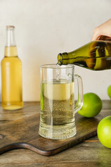 Woman pouring apple cider from bottle into glass on wooden background