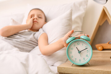 Morning of sleepy little boy turning off alarm clock