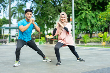 muslim couples in gym clothes doing the leg warm-up movement together before exercising in the park