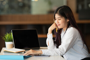 Young businesswoman holding pencil and looking at notebook while sitting at her office desk.