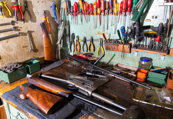 Workplace of gunsmith in professional weapons workshop with tools and disassembled shotgun during repair or maintenance