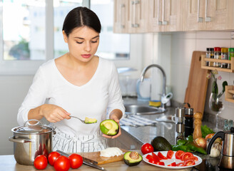 Young attractive woman standing in home kitchen, preparing vegetable dish
