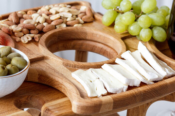 Fototapeta na wymiar Serving wooden table for wine, glasses and snacks. Handmade segmented Portion wooden table. Grapes, cheese, wine and nuts. 