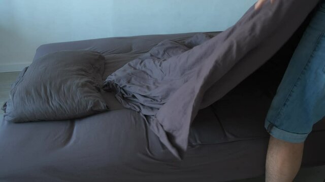 Man makes the bed in bedroom carefully spreads blanket cover on bed, closeup. Bed with pillow, warm winter blanket and brown cotton linen.