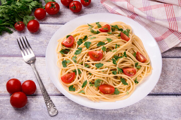 Pasta spaghetti with cherry tomatoes, fried sausage and parsley  in white plate on a light background.