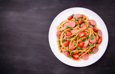 Pasta spaghetti with cherry tomatoes, fried sausage and parsley  in white plate on a black  background.