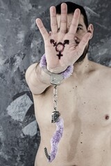The man has a symbol of the third sex drawn on his palm and handcuffs pinned to his hand. The man feels bound by the prejudices of society regarding the division of the sexes.