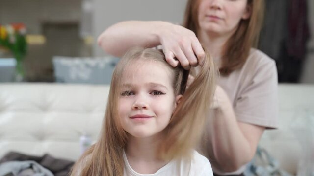 Mom combs her daughter and makes two tails, hurry, it turns out not immediately. preparing the child for the performance on stage. eye makeup.