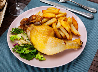 Fried chicken leg with onions served with salad and fried potatoes in a restaurant