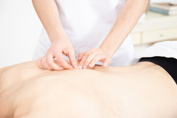 Closeup view of a physiotherapist exploring the backbone or dorsal spine of a shirtless patient.