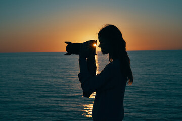 woman photographer silhouette at sunset near the sea side view
