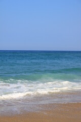 Fototapeta na wymiar La mer le ciel sont bleus, le sable fin est jaune, quelques vagues se dessinent sur l´eau devenant verte proche de la plage.