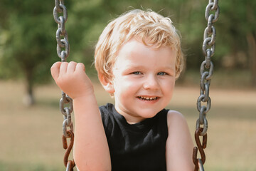 Cute little blonde boy playing on swing at playground