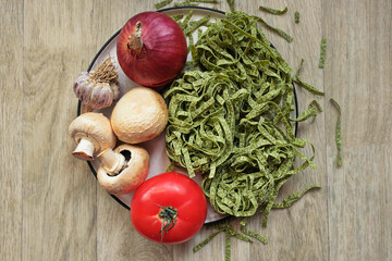 Raw green pasta fettuccine with spinach on a plate with ingredients for the preparation of national Italian dishes: tomatoes, onions, garlic,