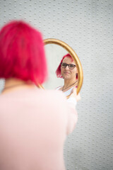 Junge Frau mit roten Haaren schaut durch einen Spiegel nachdenklich in die Ferne