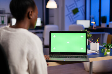 Employee with dark skin working in evening at marketing strategy using mock up green screen chroma key laptop computer with isolated display. Entrepreneur sitting at desk in business company office