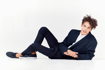 fashionable guy in a suit and sneakers sitting on the floor in a bright room curly hair model