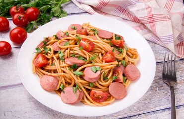 Pasta spaghetti with cherry tomatoes, fried sausage and parsley  in white plate on a light background.