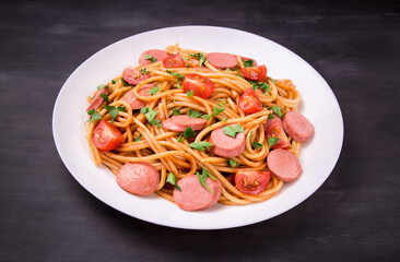 Pasta spaghetti with cherry tomatoes, fried sausage and parsley  in white plate on a black  background.