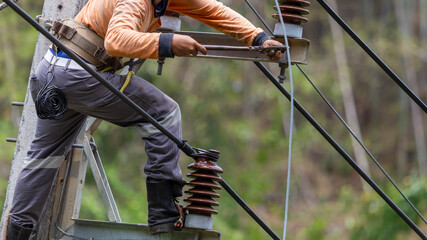 Rural electric poles are being repaired by electricians installing wires to connect. The tops of...