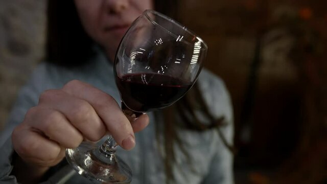 adult brunette woman is holding glass with red wine at wine-tasting, viewing color, closeup view