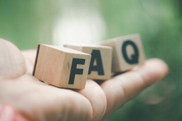 FAQ - text on wooden cubes placed on hand against nature background