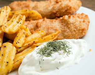 Traditional fish and chips dish with white mayo sauce and dill herbs on white plate. Common take away meal in English speaking nations. Cooked cod with peppered potato fries. Selective focus