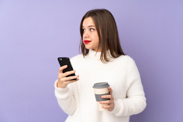 Fototapeta premium Teenager girl isolated on purple background holding coffee to take away and a mobile while thinking something