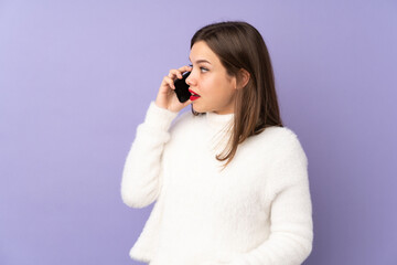 Teenager girl isolated on purple background keeping a conversation with the mobile phone with someone