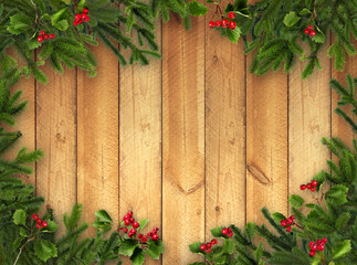 Green Christmas tree branches and red berries on warm brown wooden background
