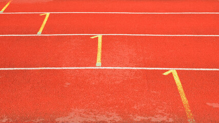 Fototapeta premium Side view of red running tracks in a street stadium. White and yellow rubberized treadmill markings.
