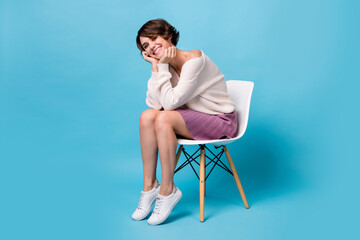 Photo portrait full body view of cute girl with head on hands sitting on chair isolated on pastel blue colored background