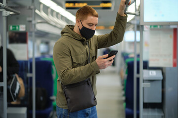 Handsome guy in respirator. man using his smartphone while traveling on the subway. He is wearing a medical mask.