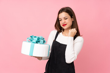 Girl holding a big cake isolated on pink background celebrating a victory