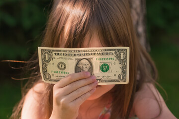 Money befor the eyes as symbol of best business motivation and desire to be rich and successful. Portrait of young beautiful girl with US Dollar bill.