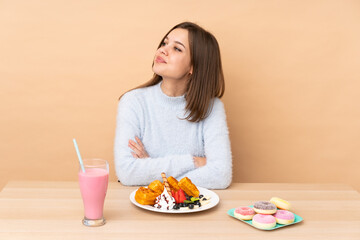 Teenager girl eating waffles isolated on beige background happy and smiling